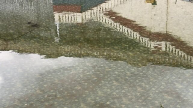 Abstract reflection of a building facade and stone steps on gently rippling water, creating fluid patterns and distorted architectural shapes