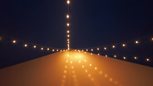 Warm string lights glowing against the night sky outside a modern event venue. Elegant outdoor decorative lighting creates a cozy atmosphere for weddings