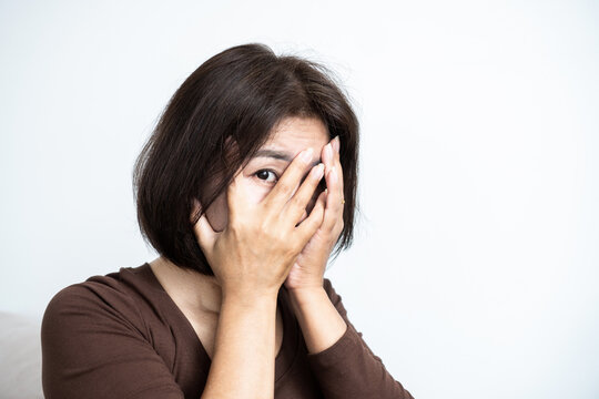 Scared Asian woman covering her face with hands and peeking through fingers in fear, shock, or shyness. Scared female feeling worried, anxious, or frightened
