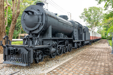 Vintage black steam locomotive with red and white carriages on display track surrounded by trees and paved path © seregraff