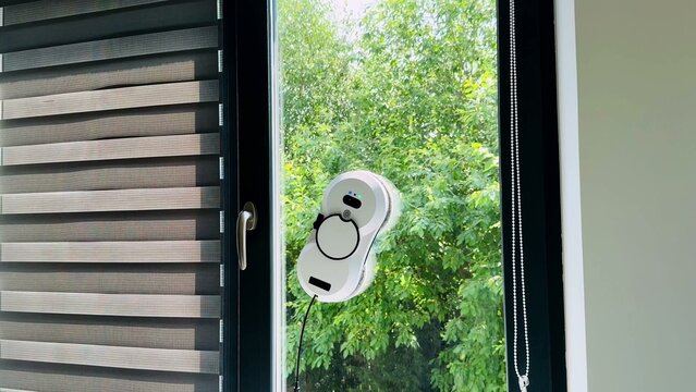 Window-mounted cleaning device on sleek glass with lush greenery in background