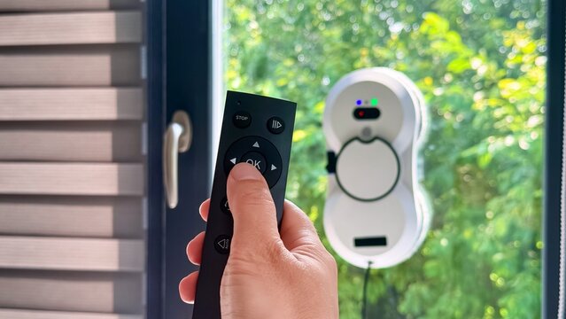 Remote control activating window cleaning robot on glass with greenery background outdoors