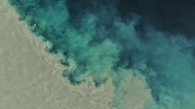 Top down aerial view of muddy sediment river water mixing with deep blue ocean current creating swirling fluid dynamic patterns