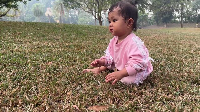 Little girl in pink sweatshirt playing with a twig on park grass