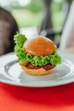Close-up of a gourmet beef cheeseburger with fresh lettuce, pickles, and cheese served on a white plate with a blurred dining background. Ideal for restaurant, fast food, and homemade burger concepts