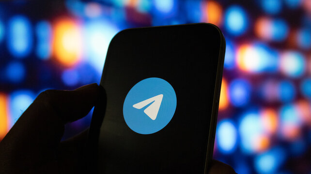 Close up shot of smartphone held in hand displaying bright telegram messenger app logo on screen.