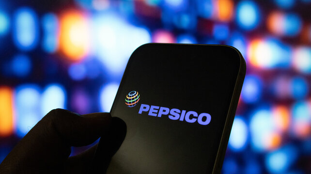 Person holding smartphone with pepsiCo logo on screen against blurred colorful background in dark.