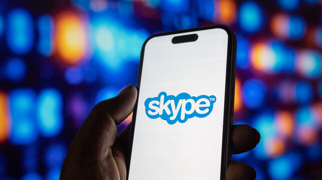 Person holding smartphone with Skype application logo on screen against blurry bokeh background.