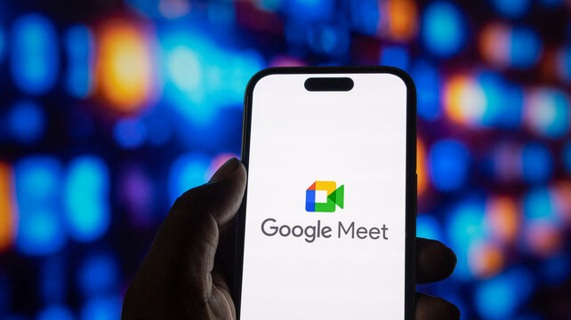 Google meet logo with text on phone screen against blurred multicolored lighting in dark setting.
