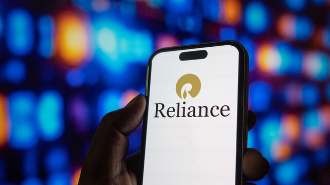 A close up shot of human hand holding smartphone with reliance industries limited logo on screen.