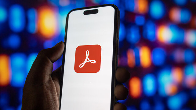 Close up of person hand holding smartphone with adobe acrobat reader app icon on screen display.