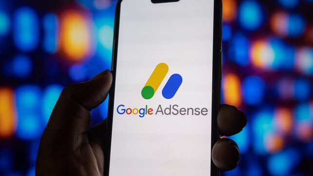 Smartphone showing google adsense logo on screen held by hand with colorful bokeh light background.