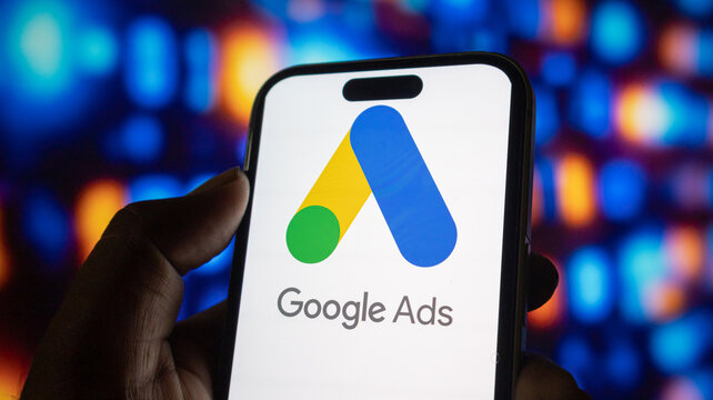 Close up of phone showing Google Ads logo with abstract bokeh lights background.