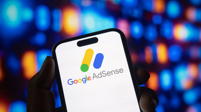 Person holding modern smartphone with google adsense digital brand logo displayed on bright screen.