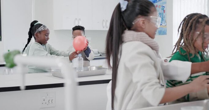 Teacher in lab coat guiding 3 youth while bubbling reaction filling green balloon on bottle