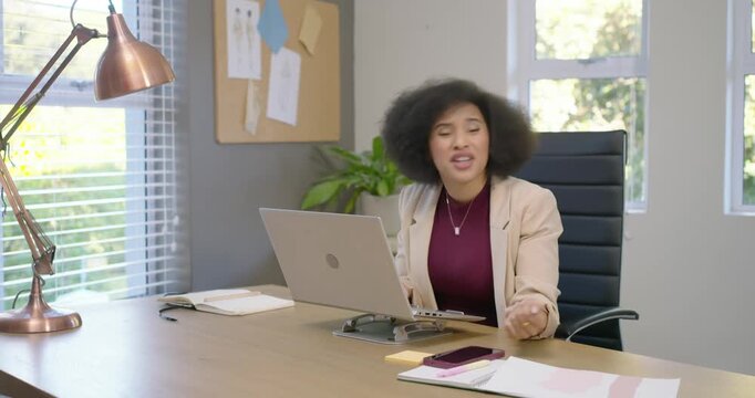 Female coworkers at desk, seated woman seeing laptop error, standing peer fixing issue in blazer
