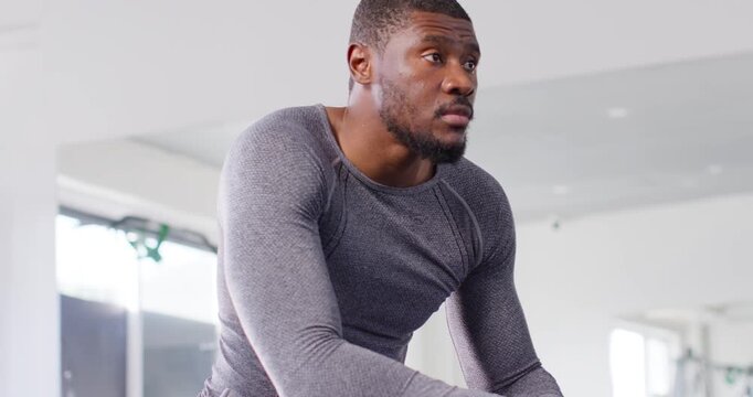 African American mid-adult man recovering from set, uncapping teal bottle and drinking on gym bench