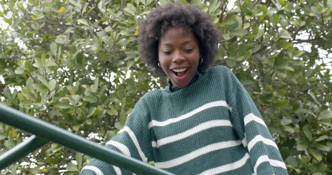 African woman leaning on green bars at playground while gazing down in striped sweater, smiling