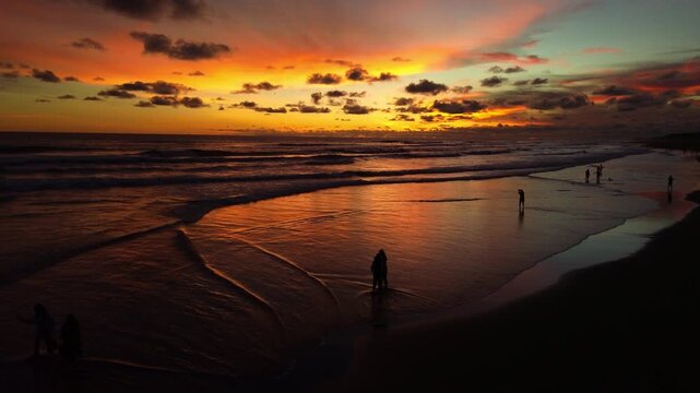 Cinematic aerial drone shot of people enjoying a vibrant golden hour sunset on Parangtritis Beach, Yogyakarta, with dramatic clouds and ocean waves.