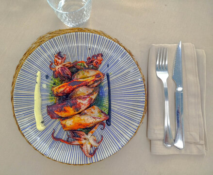 A plate of grilled baby squid, with cutlery placed on a napkin beside it