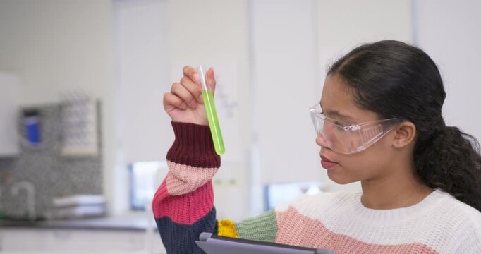 Schoolgirl in knit sweater with goggles holding test tube, checking tablet data in lab, copy space