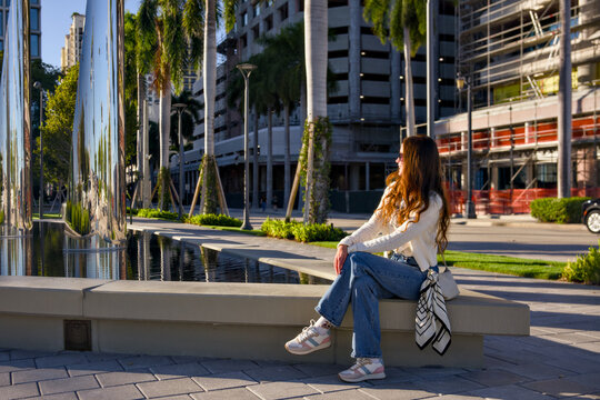 A woman relaxes on a bench in a palm lined city plaza