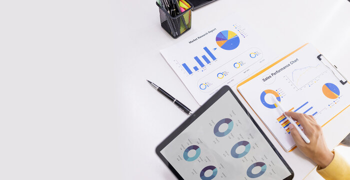 A close-up of business professionals analyzing market research reports and sales performance data using colorful charts, graphs, and a pen for pointing.