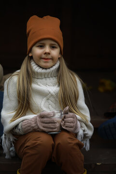 Cozy Autumn Vibes: Child Enjoying Hot Cocoa Outdoors in Warm Knit Wear