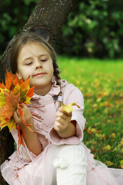 Child Holding Autumn Leaves in Park: Embracing Fall Colors and Nature in Outdoor Setting