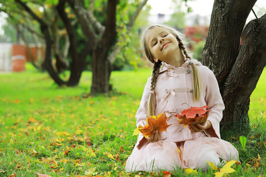 Joyful Child in Autumn Park Holding Colorful Leaves with a Playful Smile