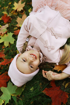 Smiling Girl in Pink Attire Lying on Autumn Leaves in a Park