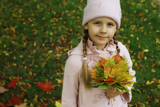 Smiling Girl Holding Autumn Leaves in a Park Wearing Pink Coat and Beanie