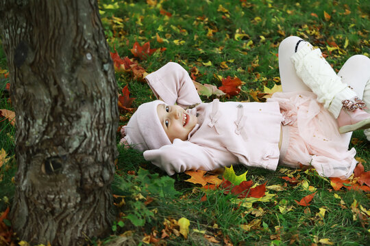 Joyful Child Relaxing in Autumn Leaves, Wearing Cozy Pink Outfit