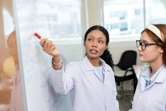 African American scientist writing on whiteboard in laboratory