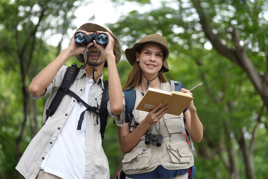 Outdoor Exploration Duo: A man and woman equipped with binoculars and a notebook venture into a lush forest, embodying the spirit of adventure and discovery.