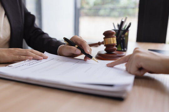 Lawyer woman signing a document with client at a desk.