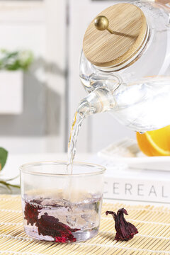 Pouring hot water into glass cup with dried hibiscus tea