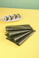 Dried seaweed sheets with sushi rolls on yellow background © LyVan