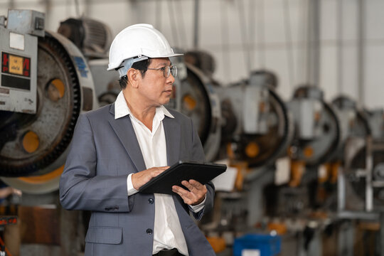 Senior Asian man in hard hat and suit standing in industrial factory
