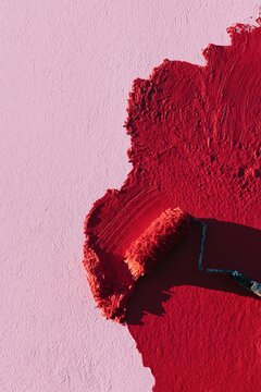 Paint roller spreading red paint over pink wall closeup for texture background and home decor design detail