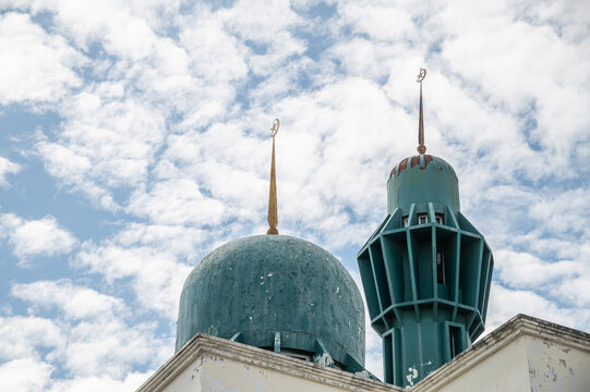 Green Mosque Domes and Minaret Spire, Islamic Architecture with Crescent Moon Finials Against Bright Blue Sky and Clouds.