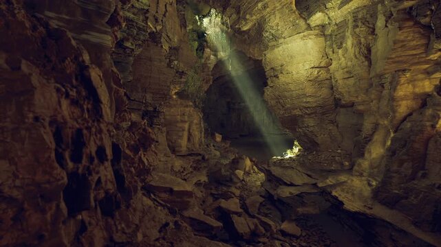 Dramatic shaft of light across cavern. Broad chamber lined with rugged boulders and mineral textures, beam highlights floating dust, atmosphere feels epic