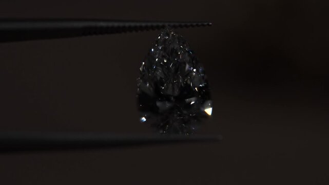 Exquisite pear-shaped diamond with swaying slightly with sparkles brilliantly in tweezers, showcasing rare luxury and investment value