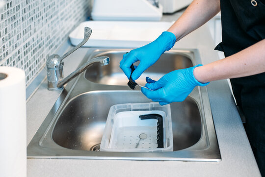 Person wearing protective gloves scrubs dental instruments over sink using small brush. Dental clinic hygiene standards, dental office cleaning protocol, autoclave sterilization dental.