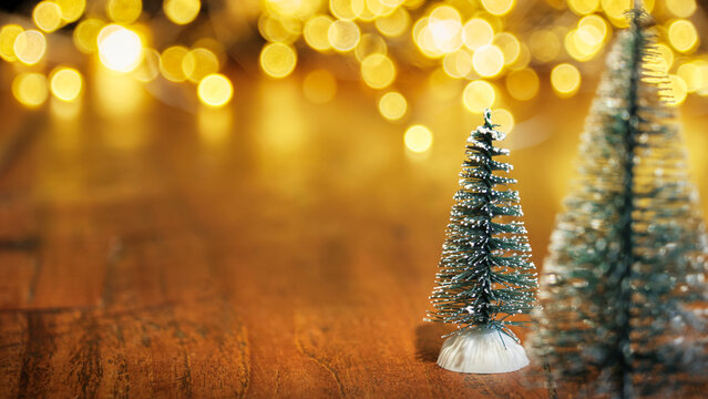 Christmas or New Year greeting card template with snow covered miniature Christmas trees and Christmas lights in the background. Xmas holidays atmosphere. Image with copy space and selective focus.
