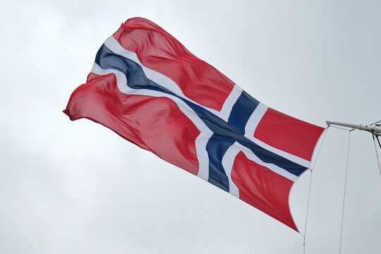A detailed view of a Norwegian flag fluttering dynamically on a boat's mast against a backdrop of overcast weather conditions