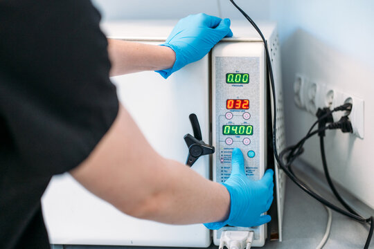 Gloved hands operate control panel of medical autoclave machine in clinic laboratory. Setting autoclave cycle, adjusting sterilization parameters, dental sterilizer control panel operation.