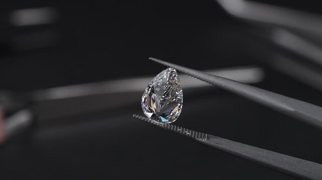 Exquisite pear-shaped diamond with swaying slightly with sparkles brilliantly in tweezers, showcasing rare luxury and investment value