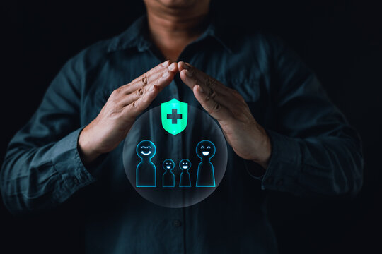 Man hands protecting a glowing digital family and green medical health shield icon. Concept of life insurance, healthcare, family security, and safety on a dark black background.