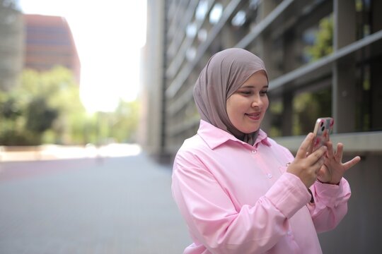 Young Muslim woman smiling at her smartphone outdoors